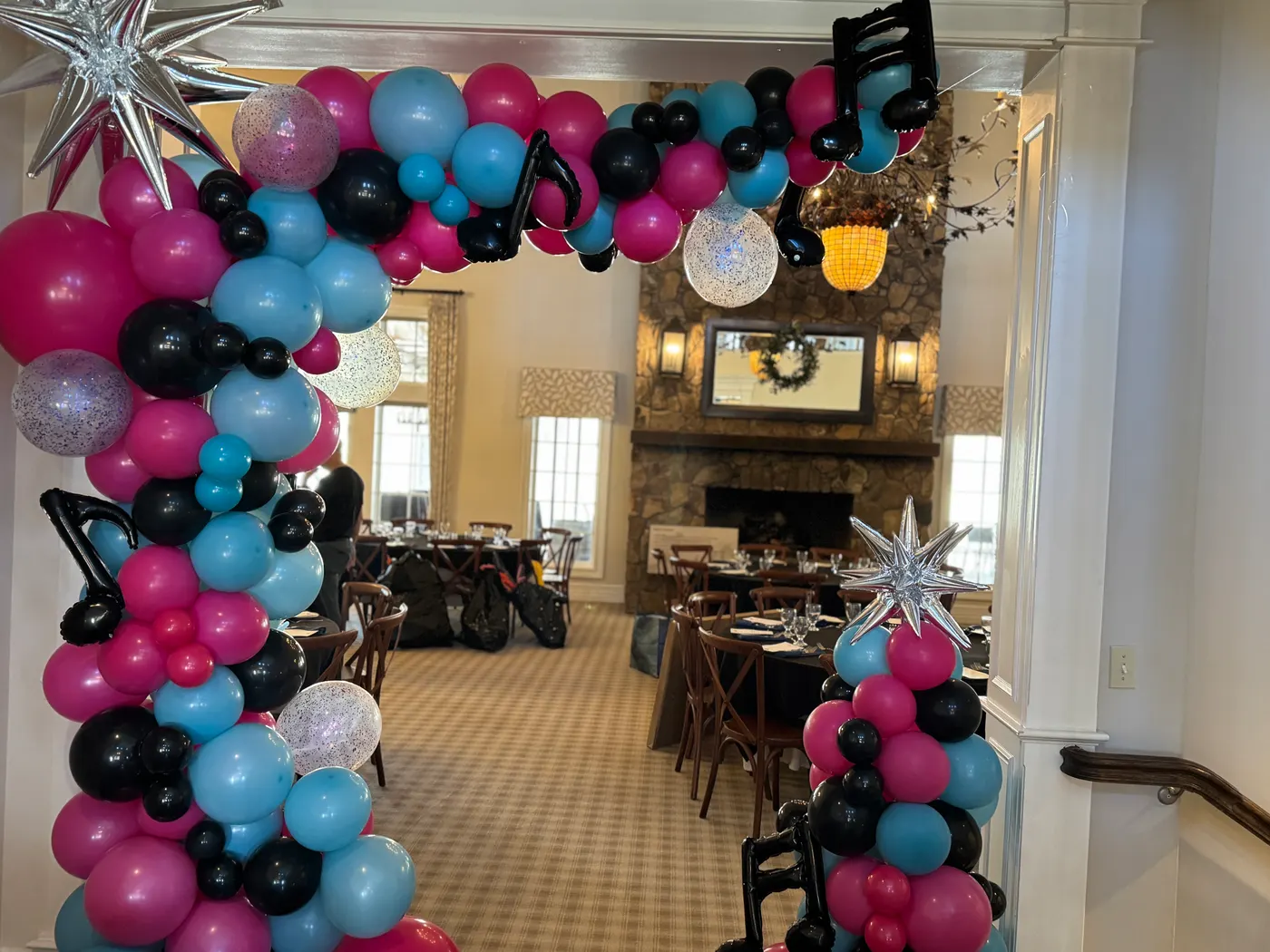 Pink, teal and black balloon arch with music notes over a restaurant entrance, designed by Party Fair Chester